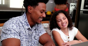 father and young daughter smiling together while using laptop at home