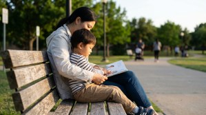 adult and young child reading picture book together on outdoor park bench